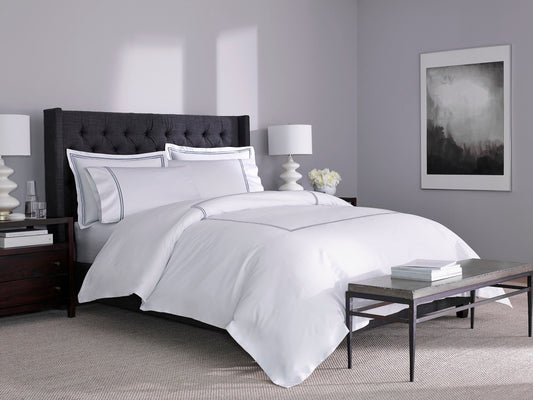 Side angle of a white cotton bed sheet with silver stitching on a bed in a modern bedroom, highlighting its breathable fabric and clean finish