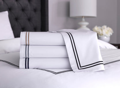Front view of folded white cotton sheets with black, silver and warm taupe stitching, highlighting their soft and silky texture and clean finish 